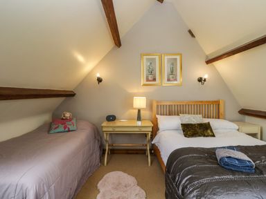 A bedroom with two beds a bedside table lamp and framed pictures at Henmarsh Cottage in Moreton-In-Marsh