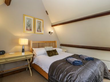 A bedroom with a wooden bed, bedside table with lamp, two framed pictures on the wall at Henmarsh Cottage in Moreton-In-Marsh