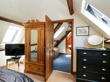 A bedroom with wooden wardrobe black chest of drawers and TV under skylights at Henmarsh Cottage in Moreton-In-Marsh