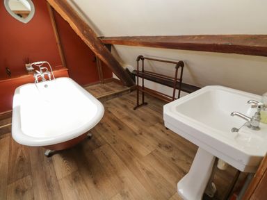 A bathroom with a freestanding bathtub sink wooden floor and exposed wooden beams at Henmarsh Cottage in Moreton-In-Marsh