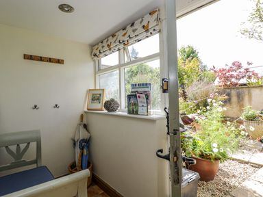 Small entry room with umbrella stand bench wall hooks and window looking onto a garden at Henmarsh Cottage in Moreton-In-Marsh