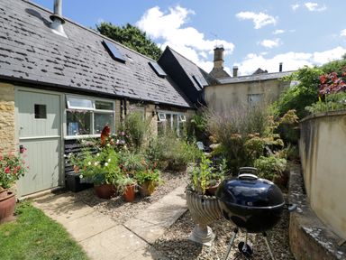 An outdoor garden area with potted plants a charcoal grill and a stone path at Henmarsh Cottage in Moreton-In-Marsh