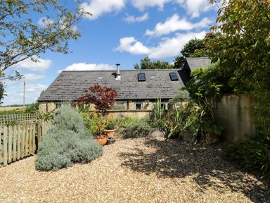 A garden area with gravel ground and various plants in front of a house with a slate roof at Henmarsh Cottage in Moreton-In-Marsh
