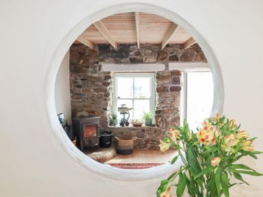 A living room with a stone wall and wood stove at Greeb Rocks Cottage in Marazion