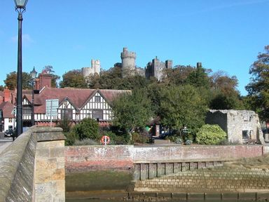 A stone bridge over a river with Tudor-style buildings and a castle on a hill in the background at The Yeoman's House in Bignor