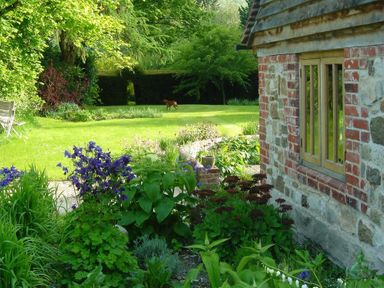 A garden with various plants and flowers next to a stone and brick building at The Yeoman's House in Bignor