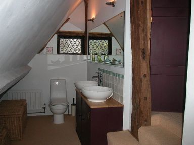 A bathroom with a toilet two sinks a mirror and wooden beams at The Yeomans House in Bignor