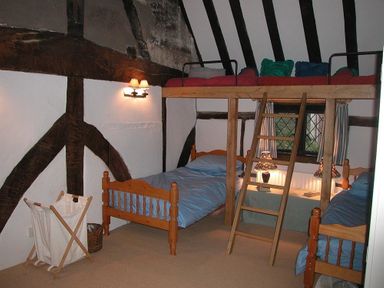 A bedroom with three single beds two on the floor and one loft bed with a wooden ladder at The Yeomans House in Bignor