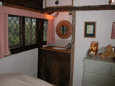 A room with diamond-pane windows with pink curtains a wooden sink unit a mirror a dresser with a teddy bear and owl ornament at The Yeoman's House in Bignor