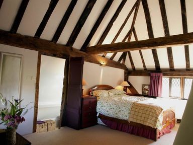 A bedroom with a bed bedside tables lamps exposed wooden beams and a window at The Yeomans House in Bignor
