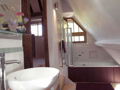 A bathroom with a white basin sink flowers on a shelf wooden beams and a bathtub under a sloped ceiling at The Yeomans House in Bignor