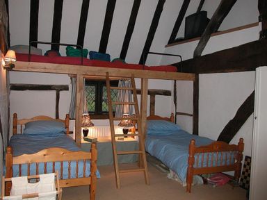 A bedroom with two single wooden beds with blue bedding and a wooden loft bed with a ladder at The Yeomans House in Bignor