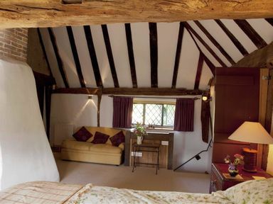 A bedroom with exposed wooden beams a sofa a small table with flowers and a window with curtains at The Yeoman's House in Bignor