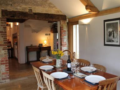 A dining room with a wooden table set with plates glasses and cutlery and a vase with flowers at The Yeoman's House in Bignor