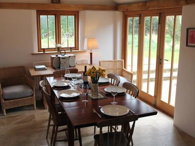 A dining room with a wooden table set for six near wooden chairs and wicker armchairs at The Yeoman's House in Bignor