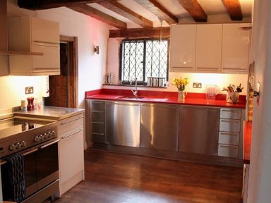 A kitchen with stainless steel appliances red countertops and wooden ceiling beams at The Yeoman's House in Bignor