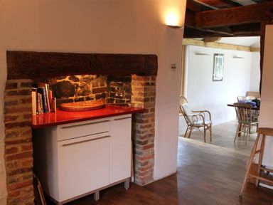 A kitchen corner with a white cabinet and red countertop inside a brick and stone alcove and a dining area with chairs and a table at The Yeomans House in Bignor