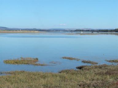 A calm body of water with grassy marshlands at the edge and distant hills and boats on the water at The Yeoman's House in Bignor