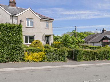 An exterior view of a semi detached house with a hedge and a garden in front at Arnant in Dolgellau