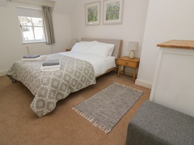 A bedroom with a double bed gray patterned bedspread bedside tables with lamps a window a rug and a gray stool at Craigluscar in Newport Pembrokeshire