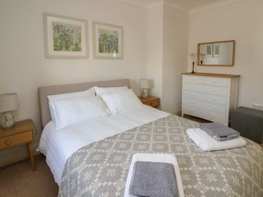 A bedroom with a double bed two bedside tables with lamps a white dresser with mirror and folded towels on the bed at Craigluscar in Newport Pembrokeshire