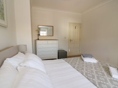 A bedroom with a made bed white dresser and a mirror at Craigluscar in Newport Pembrokeshire