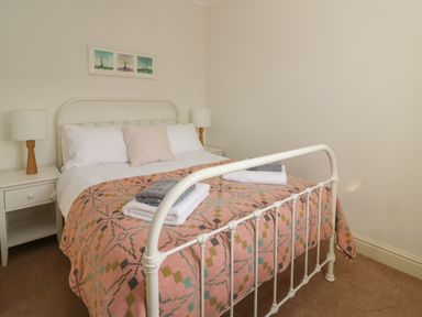 A bedroom with a white metal bed frame pink patterned blanket bedside tables and lamps at Craigluscar in Newport Pembrokeshire