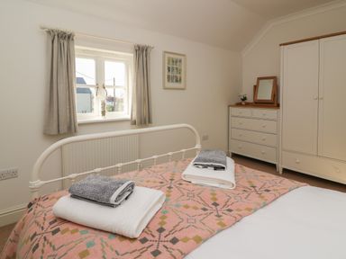 A bedroom with a bed covered by a patterned blanket two sets of folded towels on the bed a window with curtains a chest of drawers with a mirror and a wardrobe at Craigluscar in Newport Pembrokeshire