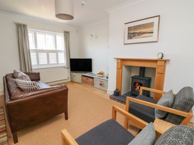 A living room with a brown leather sofa two grey armchairs a wood burning stove television and a window with curtains at Craigluscar in Newport Pembrokeshire