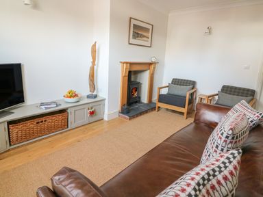 A living room with a brown leather sofa and patterned cushions two armchairs a wooden fireplace and a TV cabinet with a basket and bowl of fruit at Craigluscar in Newport Pembrokeshire