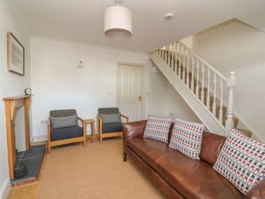 A living room with a brown leather sofa with patterned pillows two armchairs a small wooden table a wooden fireplace and a staircase at Craigluscar in Newport Pembrokeshire