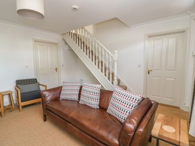 A living room with a brown leather sofa and patterned cushions a wooden armchair a staircase and two closed doors at Craigluscar in Newport Pembrokeshire
