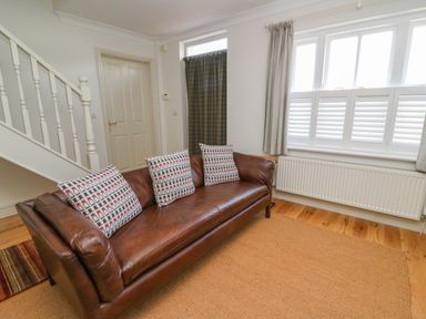 A living room with a brown leather sofa and three patterned cushions near a window with white shutters at Craigluscar in Newport Pembrokeshire