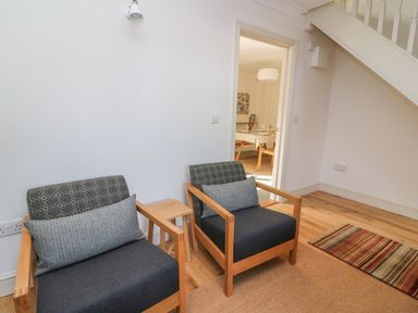 Two wooden armchairs with cushions and a small wooden stool between them in a room next to an open door showing a dining area at Craigluscar Newport Pembrokeshire
