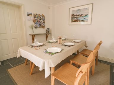 A dining room with a table set for six with plates wine glasses and wooden chairs at Craigluscar in Newport Pembrokeshire