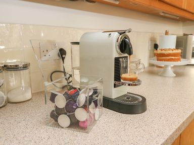 A kitchen countertop with a coffee machine pouring coffee into a glass cup and a container of coffee pods at Craigluscar in Newport Pembrokeshire
