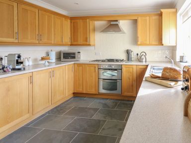 A kitchen with wooden cabinets and drawers with a microwave oven stove kettle and bread on the countertop at Craigluscar in Newport Pembrokeshire