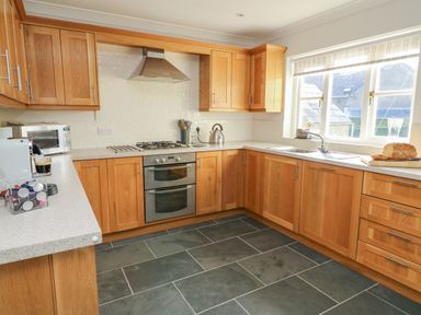 A kitchen with wooden cabinets a stove oven a sink by the window and a coffee machine on the counter at Craigluscar in Newport Pembrokeshire