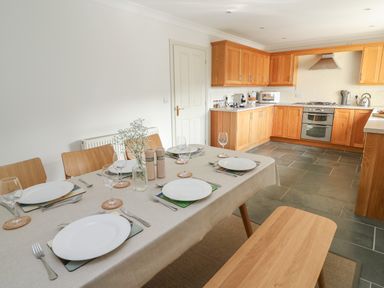 A dining table set for six with plates glasses and cutlery next to a kitchen with wooden cabinets and tiled floor at Craigluscar in Newport Pembrokeshire