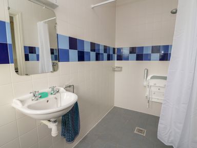 A bathroom with a sink mirror tiled walls and a shower area with curtain at Craigluscar Newport Pembrokeshire