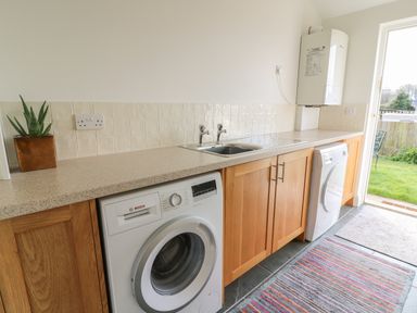 A laundry room with washing machine dryer sink wooden cabinets and a door to a garden at Craigluscar in Newport Pembrokeshire