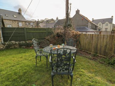 A garden with a metal table and four chairs with cups and plates on the table at Craigluscar Newport Pembrokeshire