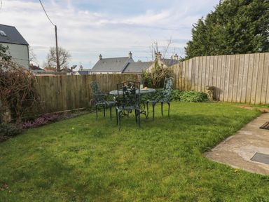 A garden with a metal table and four chairs on the grass surrounded by wooden fences at Craigluscar in Newport Pembrokeshire