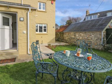 A garden with a metal table and chairs with cups and cake near a yellow house at Craigluscar in Newport Pembrokeshire