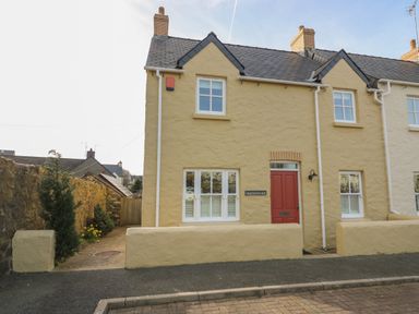 A yellow stone house with a red door and white windows at Craigluscar in Newport Pembrokeshire