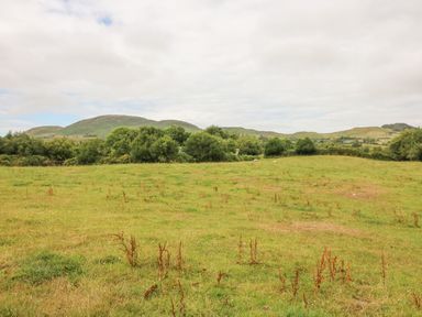 A grassy field with bushes and hills in the background at Dromstabla in Glencar