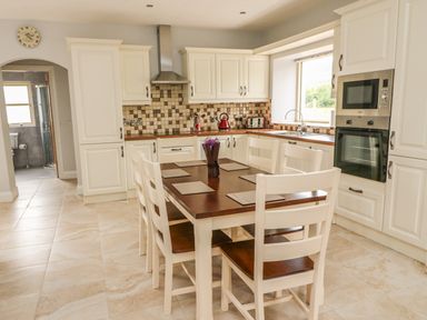 A kitchen with a wooden dining table and white chairs next to white cabinets with built in appliances at Dromstabla in Glencar
