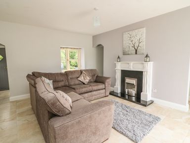 A living room with a brown sectional sofa a fireplace with decor and a gray rug on tiled floor at Dromstabla in Glencar