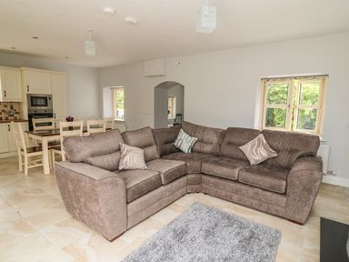 An open living area with a brown L-shaped sofa and pillows near two windows and a dining table with chairs at Dromstabla in Glencar