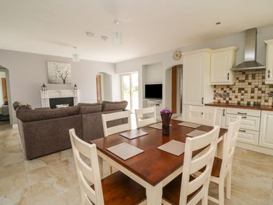 A kitchen and dining area with a wooden table and white chairs and a living room with a brown sofa and fireplace at Dromstabla in Glencar